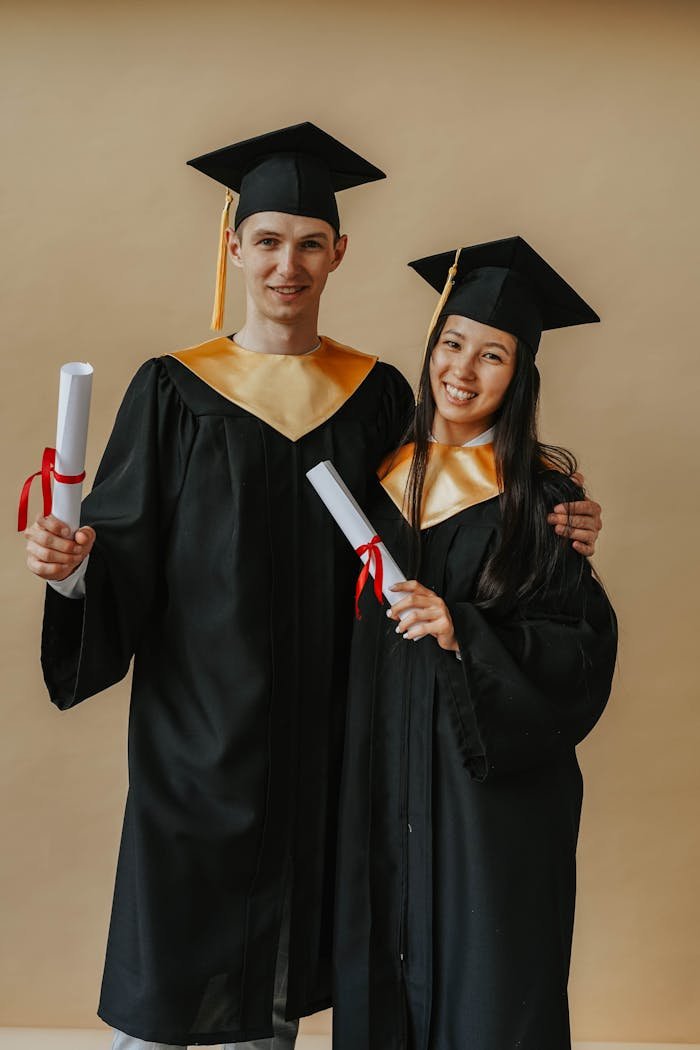 A smiling duo in graduation gowns, celebrating their academic success with diplomas.
